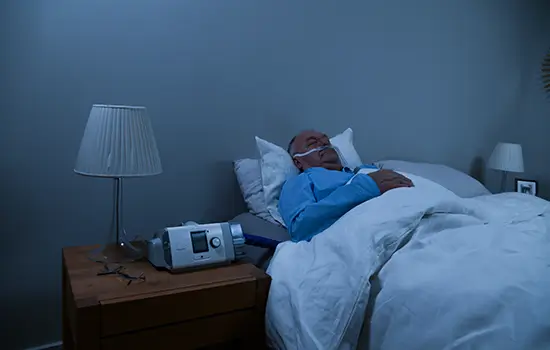 Hombre durmiendo con una máquina Resmed en la cabecera de la cama.