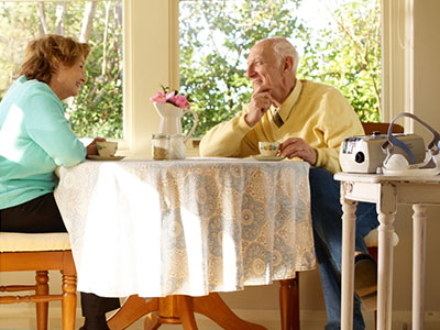 Pareja de ancianos tomando café o té, sentados en una mesa. Podemos ver un dispositivo ResMed en otra mesa al lado.