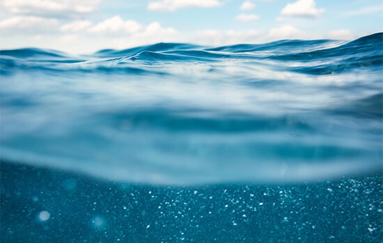 Fotografía de las olas del océano con cielo azul, tomada desde debajo del agua.