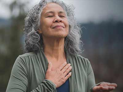 Mujer canosa inspira con la mano en el corazón